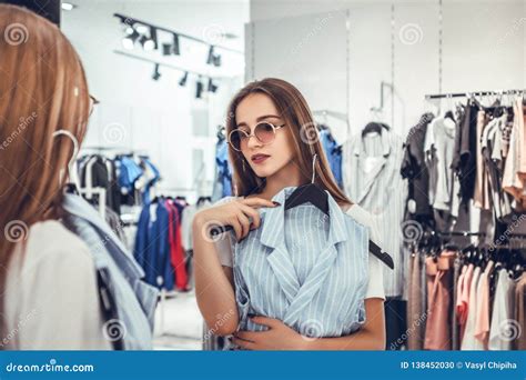 Happy Woman Choosing Clothes And Looking To Mirror In Mall Or Clothing