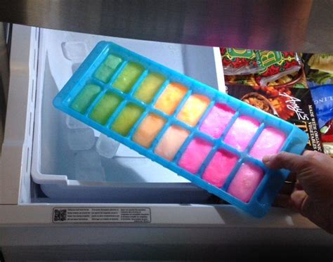 A Person Is Holding An Ice Tray In Front Of A Freezer With Food Inside