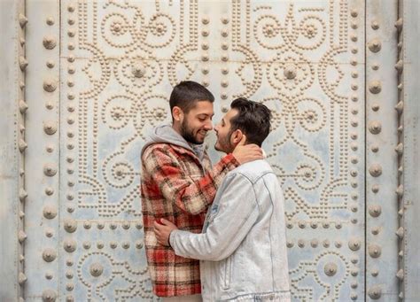 Pareja joven gay sonriendo confiados abrazándose unos a otros en la calle Foto Premium