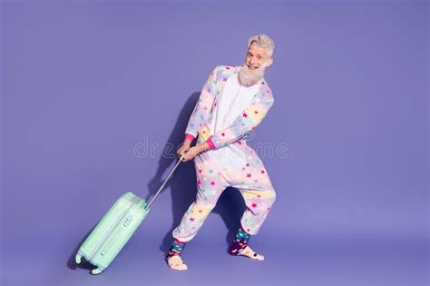 Joyful Mature Man In Colorful Unicorn Pajama Posing With Suitcase Against Vibrant Violet