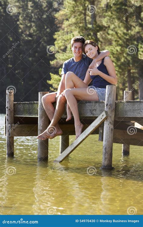 Young Romantic Couple Sitting On Wooden Jetty Looking Out Over Lake