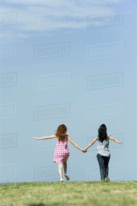 Two Young Women Walking Hand In Hand Outdoors Rear View Stock Photo