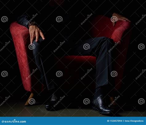 Male Businessman In A Black Suit Sitting In Red Chair Black Background