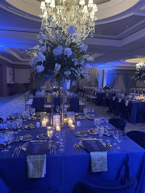 A Table Is Set With Blue Linens And Silver Place Settings For An