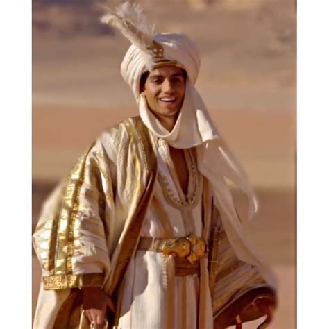 A Man Dressed In White And Gold Holding A Red Bag While Standing On Top Of A Desert