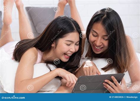 Asian Lesbian Couple Lying Down On Bed Using Tablet Browsing Internet In Morning At Cozy Home