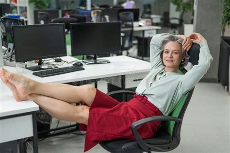 Mature Caucasian Woman Took Off Her Shoes And Put Her Feet On The Desktop In The Office Stock