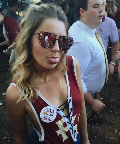 A Woman With Her Tongue Out Wearing Sunglasses And A Tank Top At A