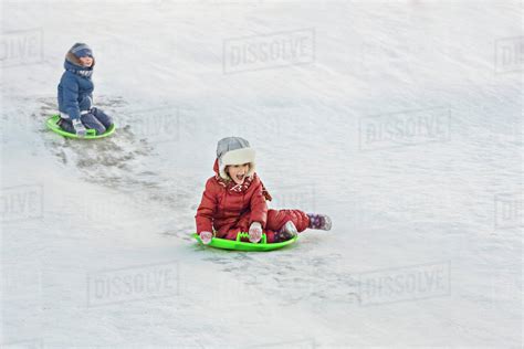 Full Length Of Siblings Tobogganing In Snow Stock Photo Dissolve