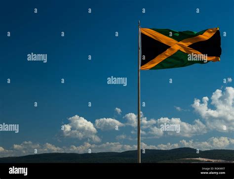 A large Jamaican flag fling in a stiff coastal breeze with blue sky in the background. Flag of ...