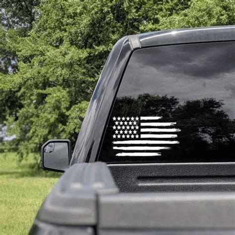 An American Flag Sticker Is On The Back Of A Pick Up Truck In Front Of Some Trees