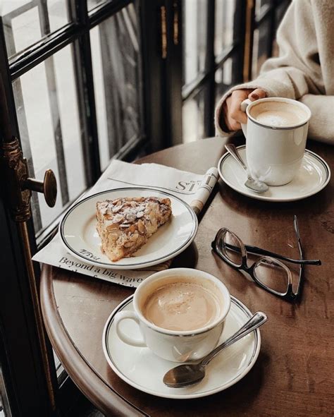 Two Cups Of Coffee Sit On A Table With Pastries And Glasses Next To Them