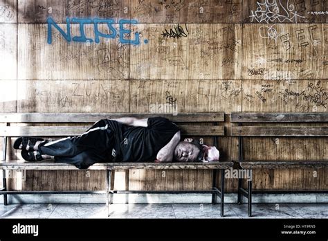 Homeless Man Sleeping On The Wooden Bench In The Train Station Stock