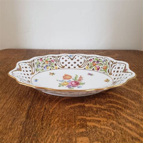 A White And Gold Serving Dish With Flowers On It Sitting On A Wooden