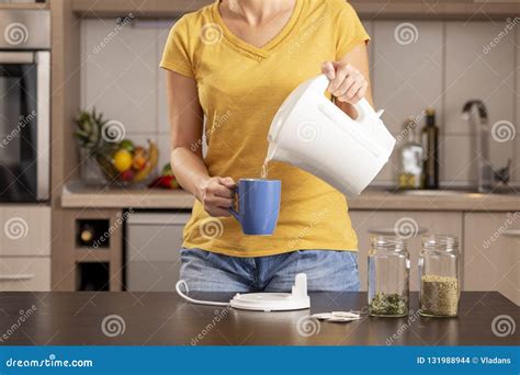 Woman Pouring Boiling Water From A Kettle Into A Tea Cup Stock Photo