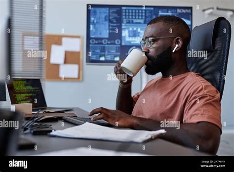 Side View Portrait Of Black Man Drinking Coffee At Workplace While