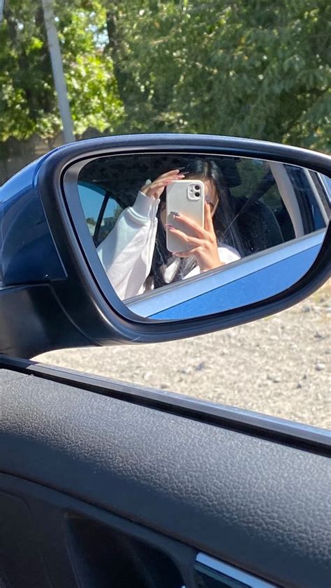 A Woman Taking A Selfie In The Side View Mirror Of A Car With Her Cell