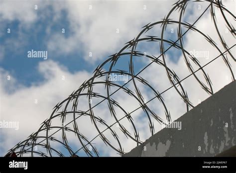 Chain Link Fence With Barbed Wire And Razor Wire Against The Blue Sky