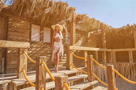 Sexy Woman Wearing Bikini Standing At Lounger Under Straw Canopy At