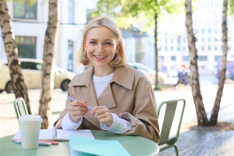 Image d une jeune femme blonde dans une tranchée élégante assise dans un café en plein air