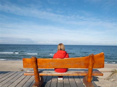 Premium Photo Woman In Red Coat Sits On The Bench Faced To The Sea