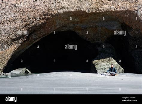 A Tourist Meditates In A Sea Cave On Wharariki Beach New Zealand