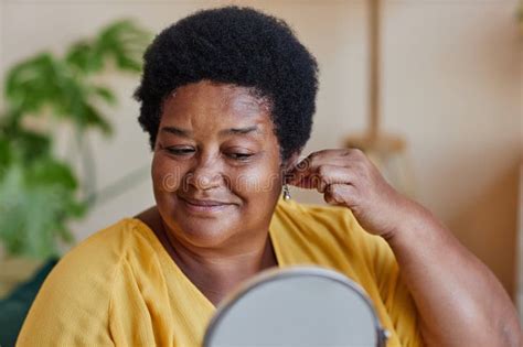 Smiling Mature Woman Trying On Small Pearl Earrings In Front Of Mirror