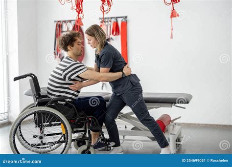 Nurse Of The Rehabilitation Center Helps Man To Get Up From A Wheelchair At Clinic Stock Image