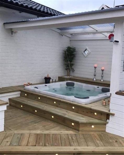 A Hot Tub Sitting On Top Of A Wooden Deck Next To A White Building With