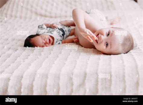 Ältere Bruder blonde junge Sohn mit kleinen Baby Schwester mit schwarzen Haaren auf dem Bett zu