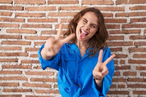 Beautiful Brunette Woman Standing Over Bricks Wall Smiling With Tongue Out Showing Fingers Of