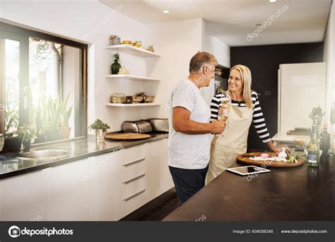 Mature Couple Cooking Drinking Wine Preparing Meal Together While Bonding Stock Photo
