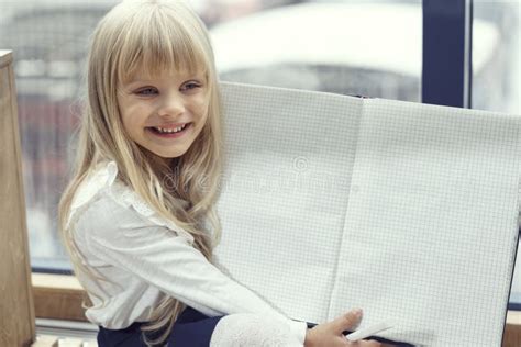 La Jolie Petite Fille Blonde Sourit Et Affiche Un Carnet Dévoilé Avec Des Pages Blanches Lieu