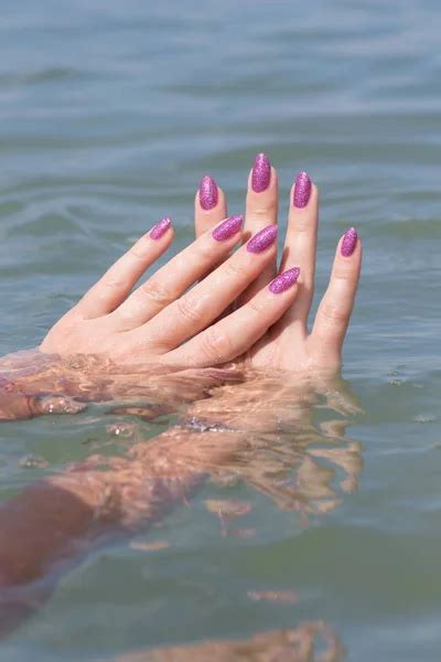 Female Hands With Pink Nails In Sea Water And Splashes Stock Image