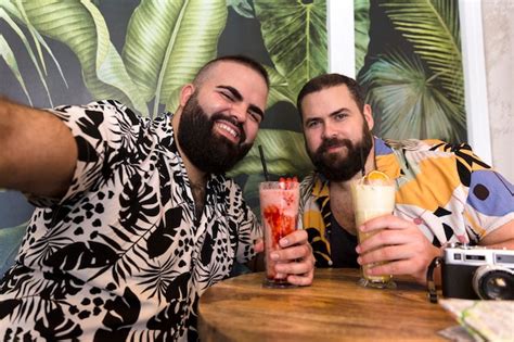Feliz pareja gay joven en ropa de verano tomando un autorretrato juntos mientras toman un cóctel