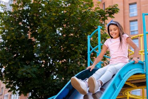 Fille Heureuse Glisse Sur Un Toboggan Dans Une Aire De Jeux Photo