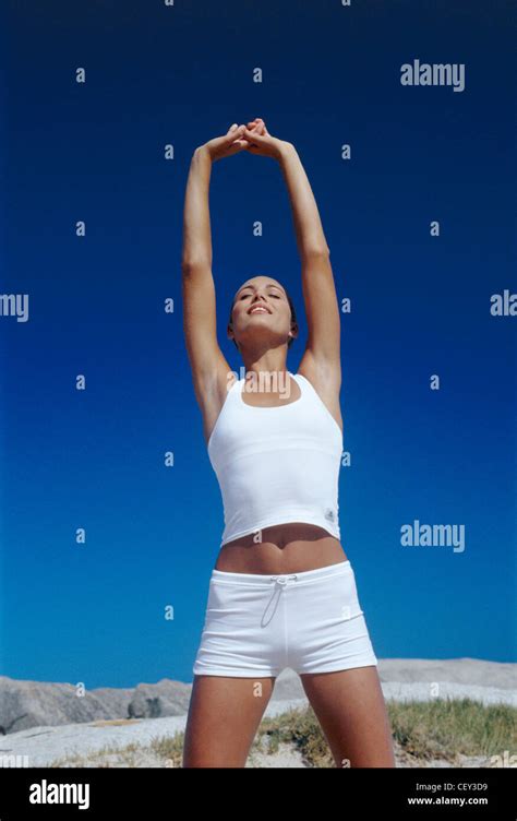 Female Brunette Hair Off Face Wearing White Vest Top And White Hot Pants Standing Arms Raised