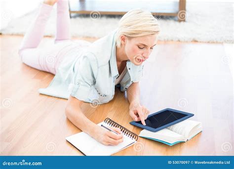 Pretty Blonde Woman Lying On The Floor And Taking Notes While Using Her Tablet Stock Image