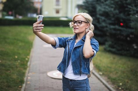 Élégant heureux jolie mode fille blonde femme en suite de jeans fait selfie sur son téléphone
