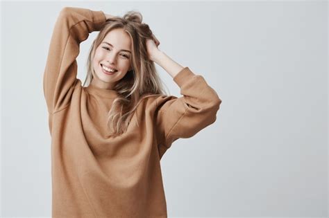 Schöne hübsche charmante junge blonde frau im losen pullover der glücklich lächelt spaß