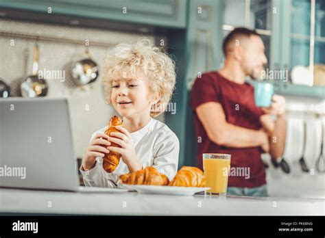 Cute Blonde Haired Boy Eating Croissant And Watching Cartoons Stock Photo Alamy