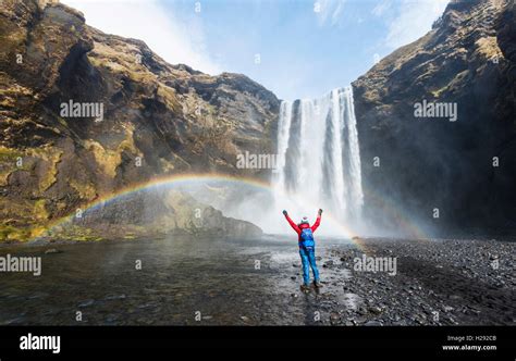 Hiker in front of Skógafoss waterfall with arms outstretched, rainbow, Skogar, Southern Region ...