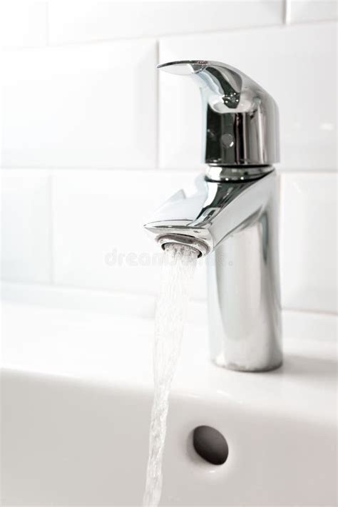 Water Flowing From The Tap Into White Ceramic Sink And White Tile Wall