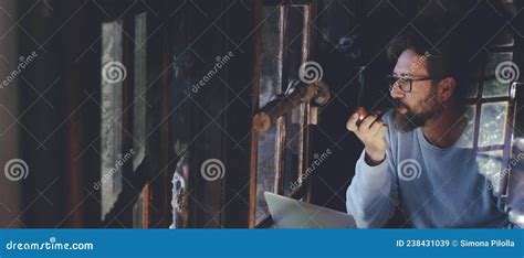 Mature Man At Work On Laptop Computer Sitting At The Table Inside A Home Cozy Cabin With Wooden