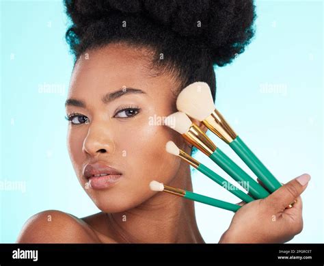 Portrait, brushes and black woman with makeup, foundation and glow against a blue studio ...