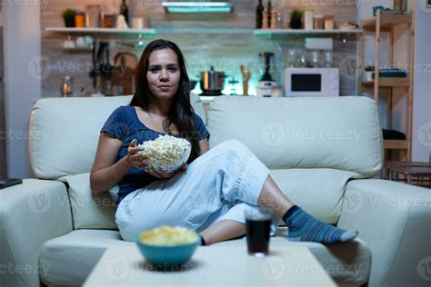 Young lady in pijamas watching Tv in living room sitting on sofa. Bored ...