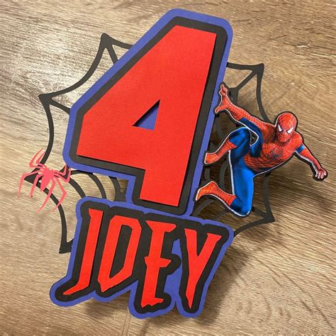 The Number Four Is Placed Next To A Spiderman Cake Topper On A Table