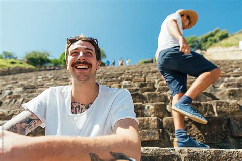 Young Smiling Man Sitting On Stone Stairs With His Friends On