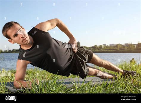 Sporty Man Doing Side Plank Exercise On Green Grass Near River Stock