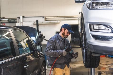 Car Mechanic At Work Changing Car Wheel Of Lifted Vehicle With